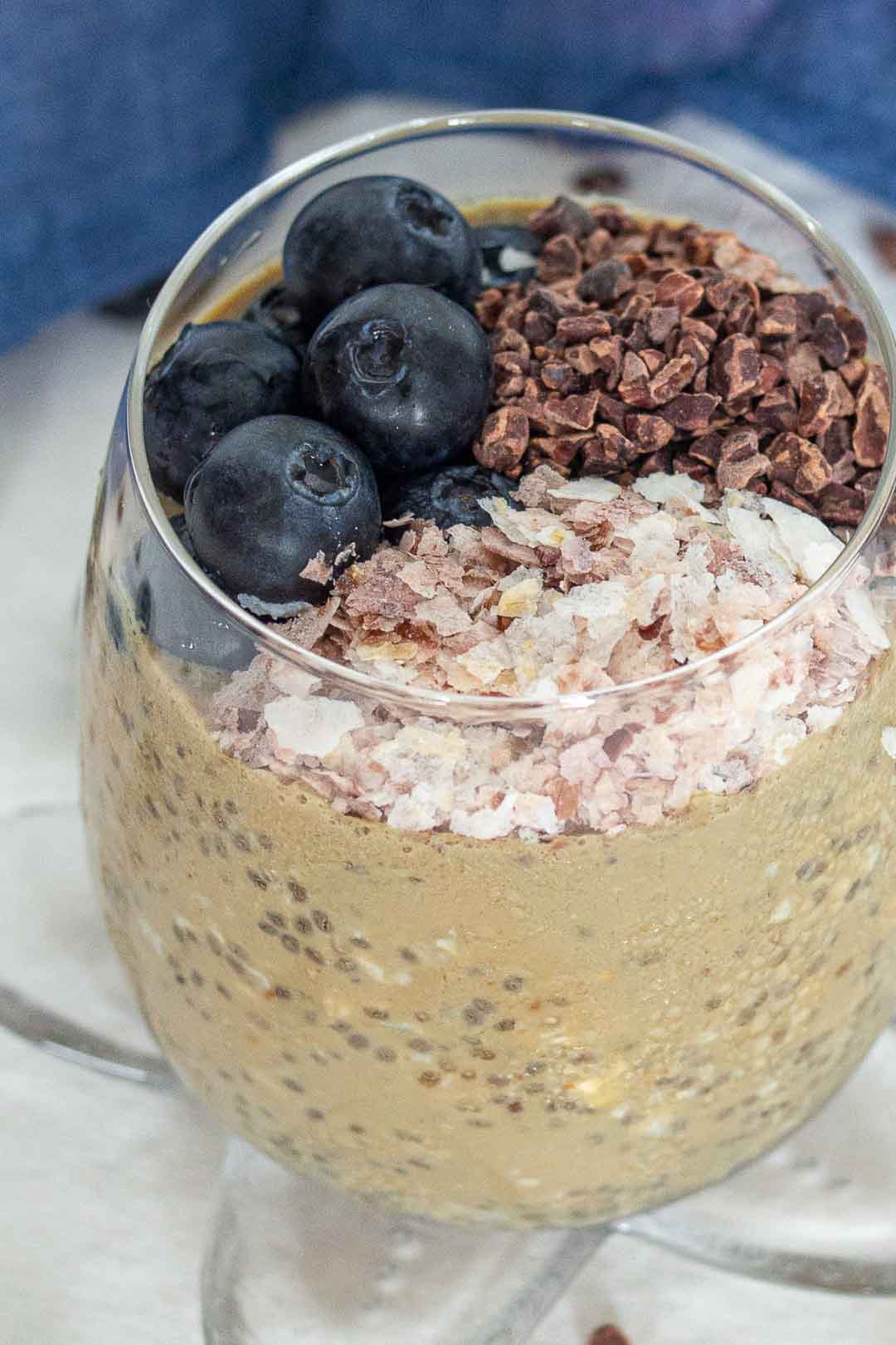 a close up of overnight oats with cacao nibs, blueberries and brown rice flakes in a glass