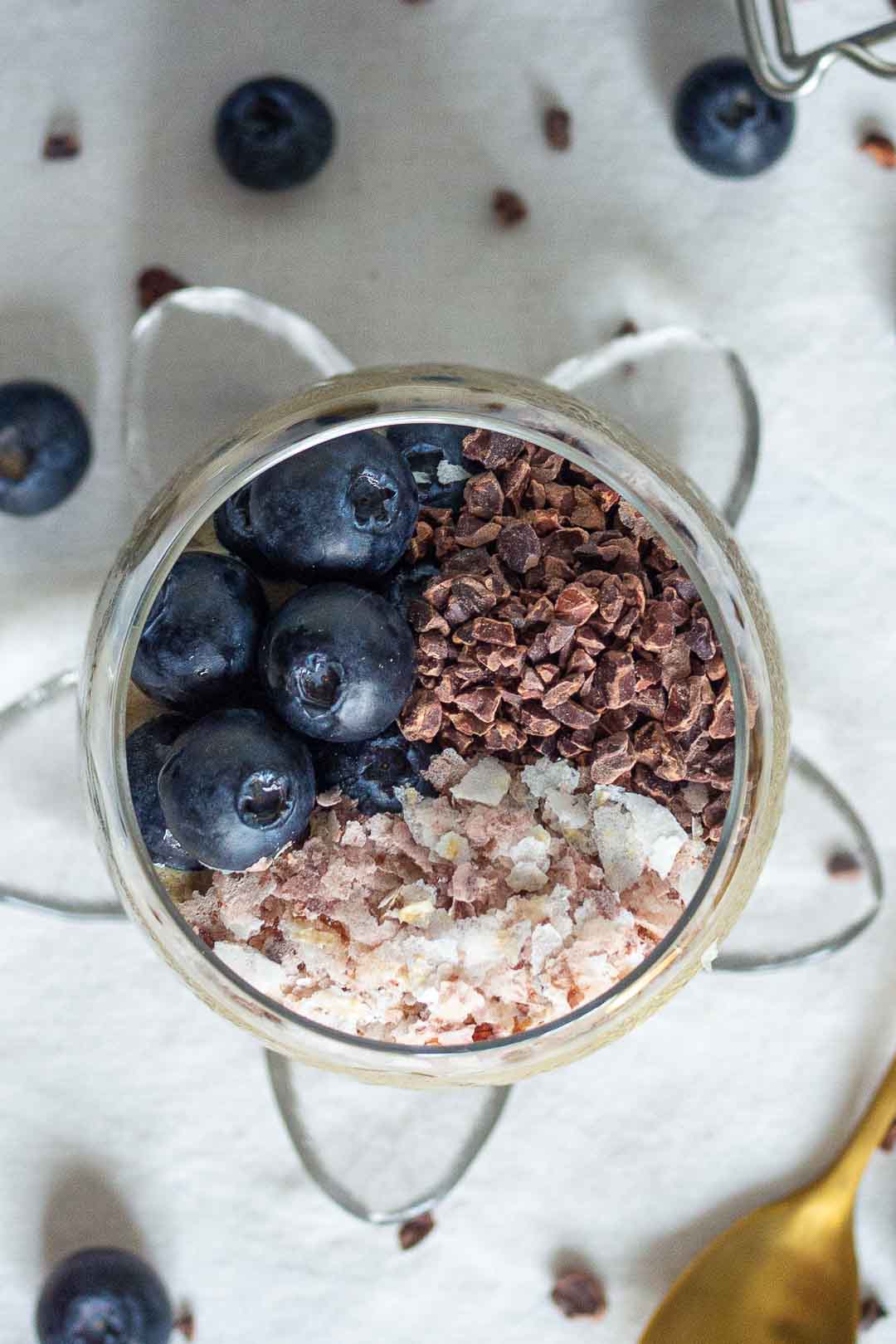 top view of a glass with cocoa nibs, brown rice flakes and blueberries inside