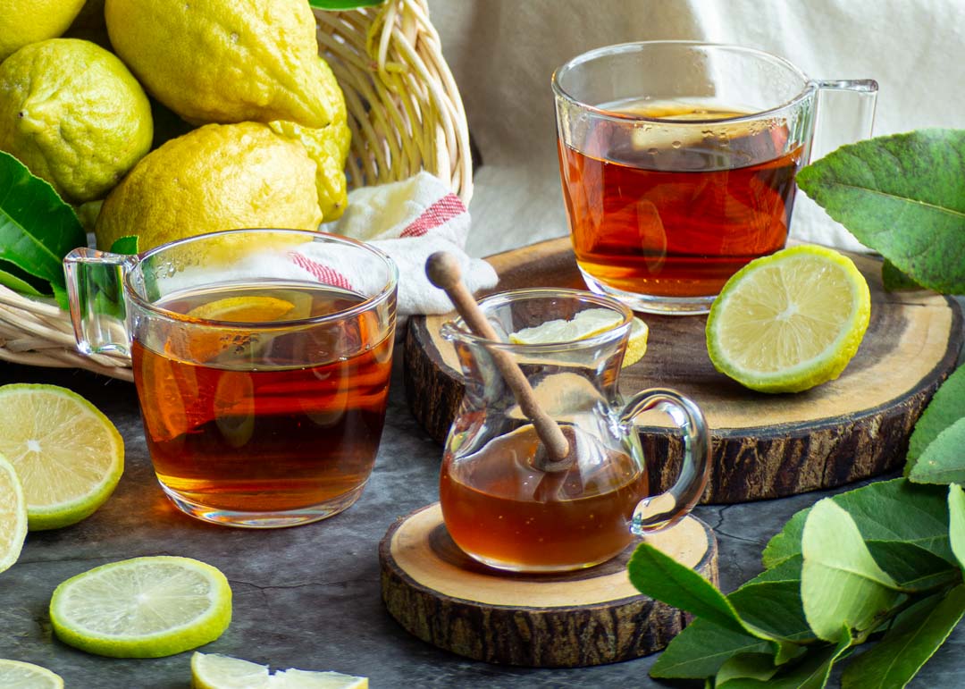 two cups of honey and lemon tea with a jar of honey and lemons in a basket