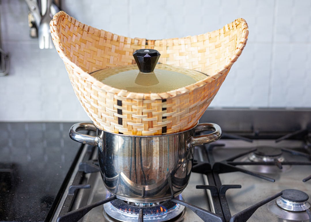 A pot on stove with a bamboo steamer basket on top of it