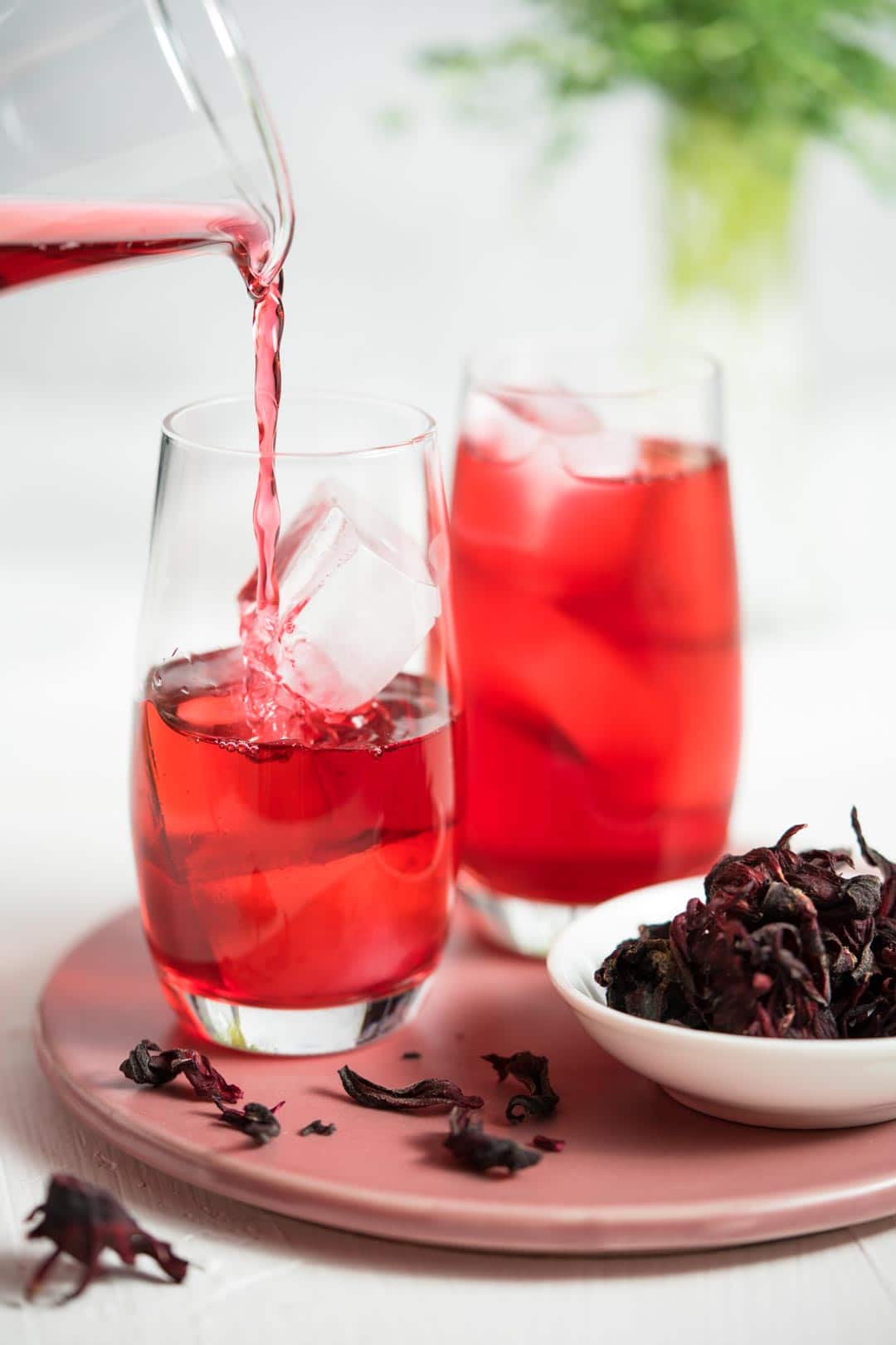 hibiscus tea being poured into a glass filled with ice cubes