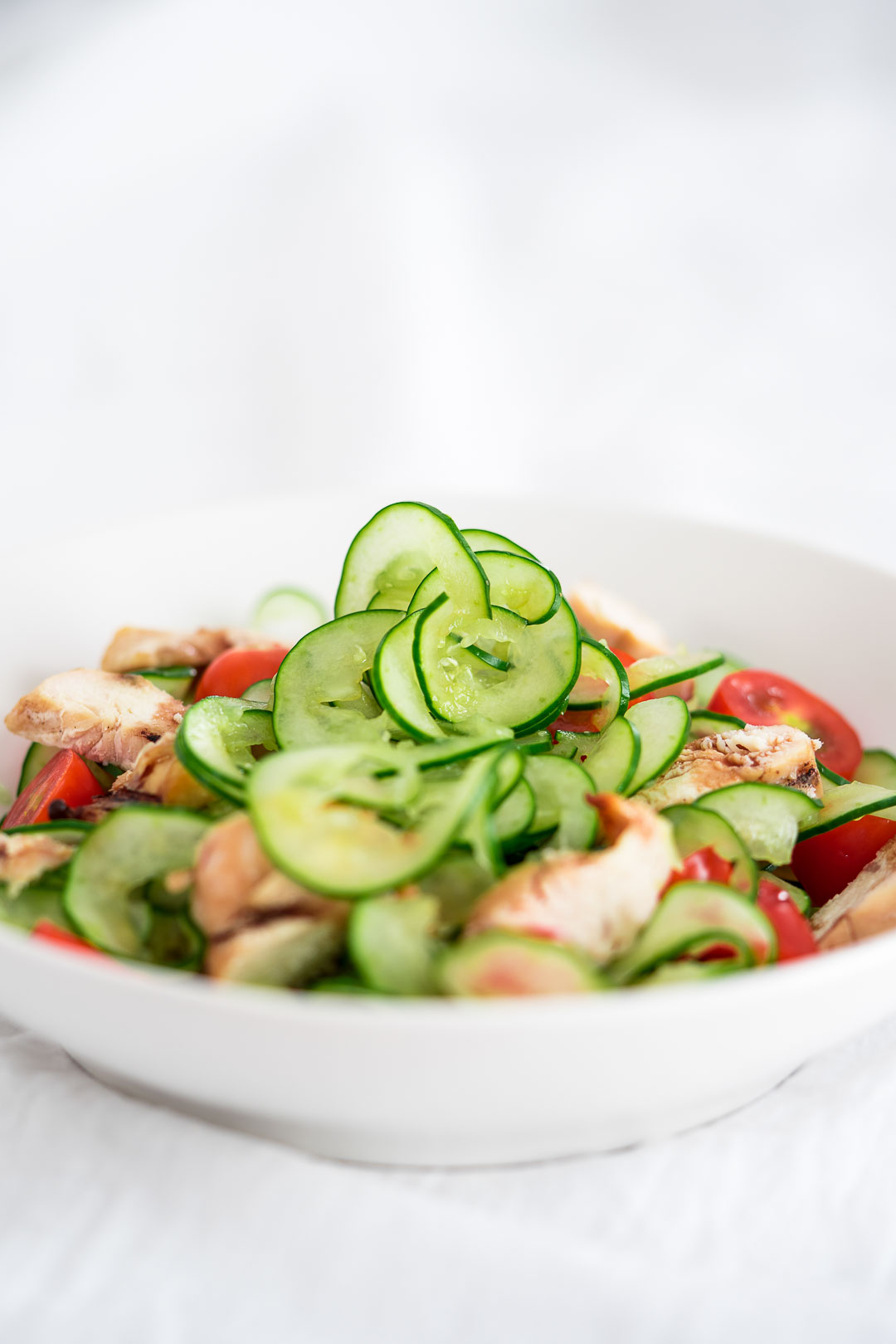 spiralized cucumber salad with tomatoes and chicken in a white dish