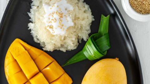 Thai mango sticky rice dessert with pandan leaves on a black plate