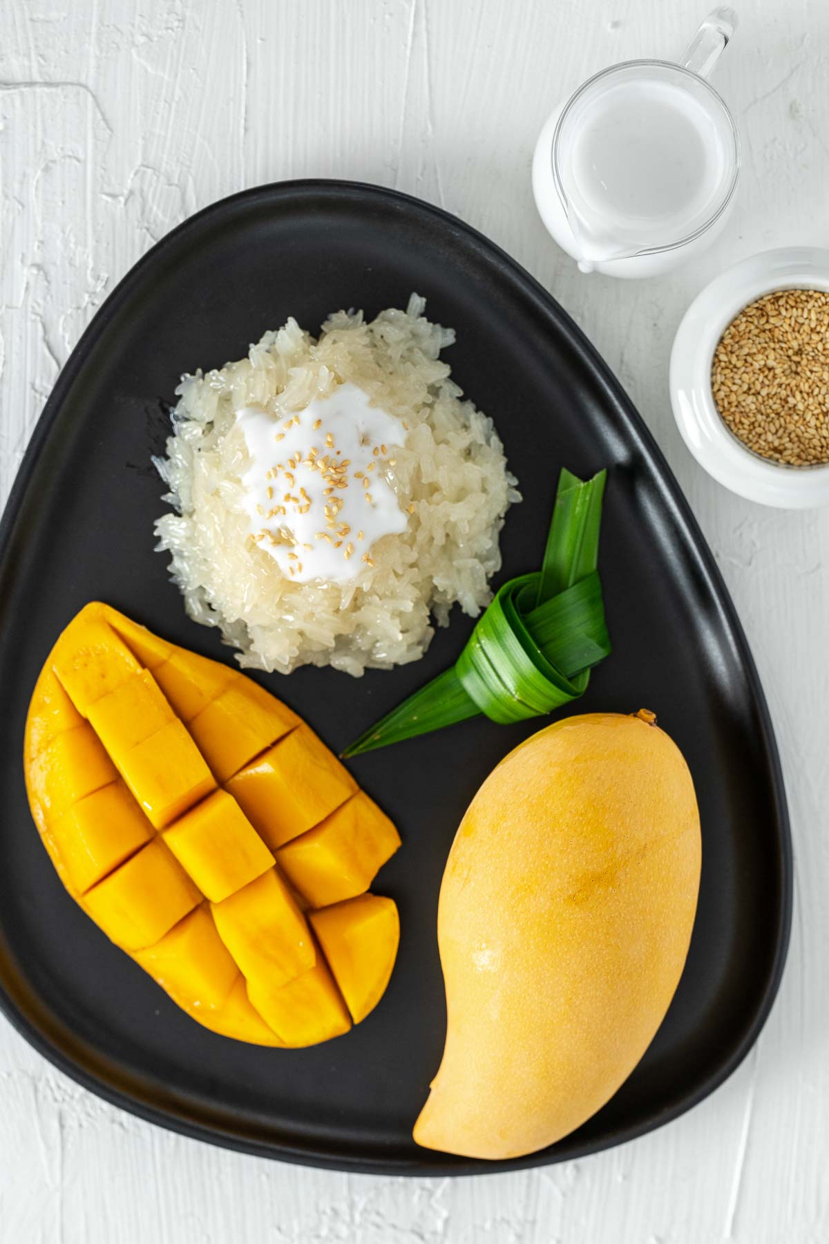 Thai mango sticky rice dessert with pandan leaves on a black plate