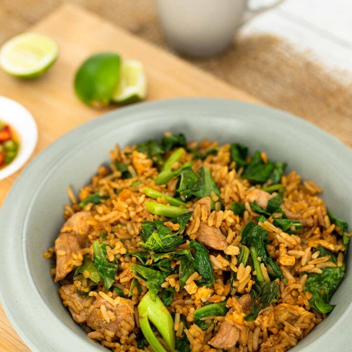 Thai pork fried rice with collards in a gray bowl on a wooden chopping board