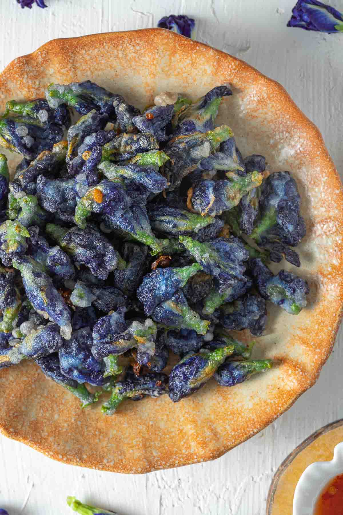 crispy deep fried butterfly pea flowers in a dish served with sweet chili sauce