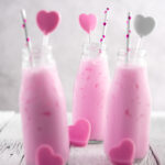 three bottles of Thai pink milk on a white wooden surface