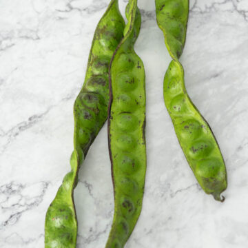 three fresh stink bean pods on a marble surface